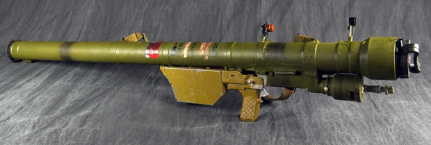 A green, shoulder-fired surface-to-air missile launcher with its gripstock and trigger mechanism is displayed against a dark fabric background.